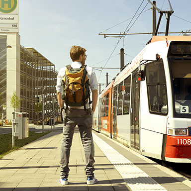 Mann mit Rucksack steht an Straßenbahn-Haltestelle